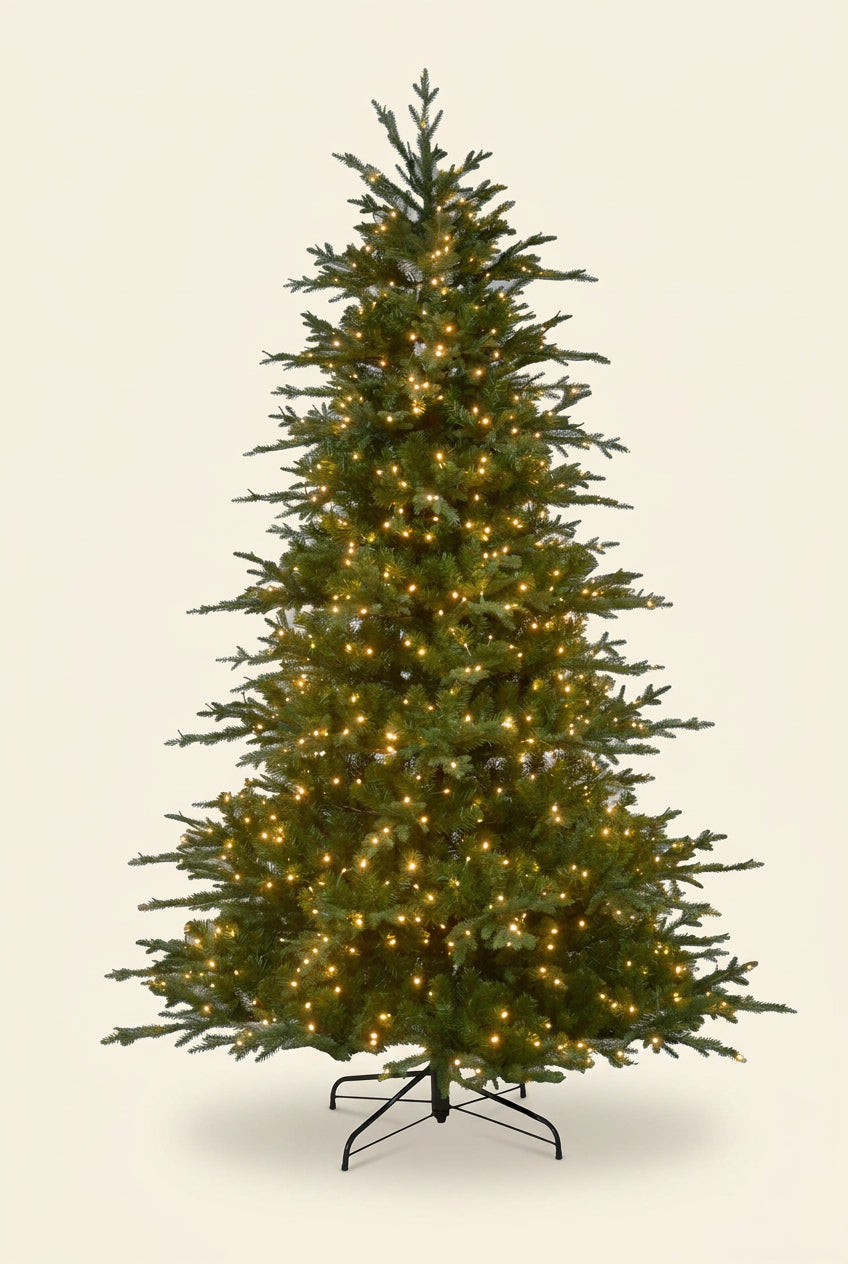 A pre-lit artificial Christmas tree with green needles and warm white lights, standing on a black metal stand against a plain white background.