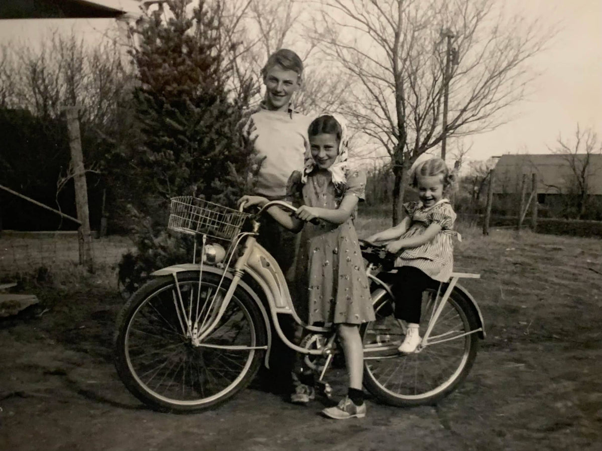 Black and white photo of Nelson children with two young girls on a bike and a teenage boy holding a Christmas tree.